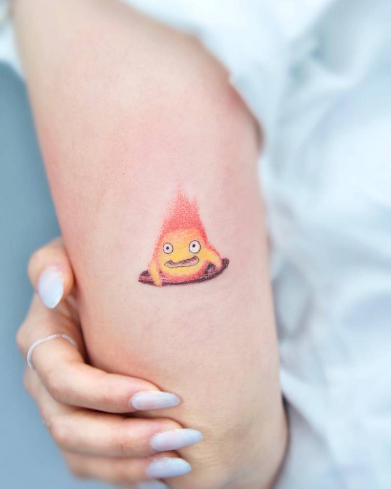 Cartoon style Calcifer tattoo located on the tricep.