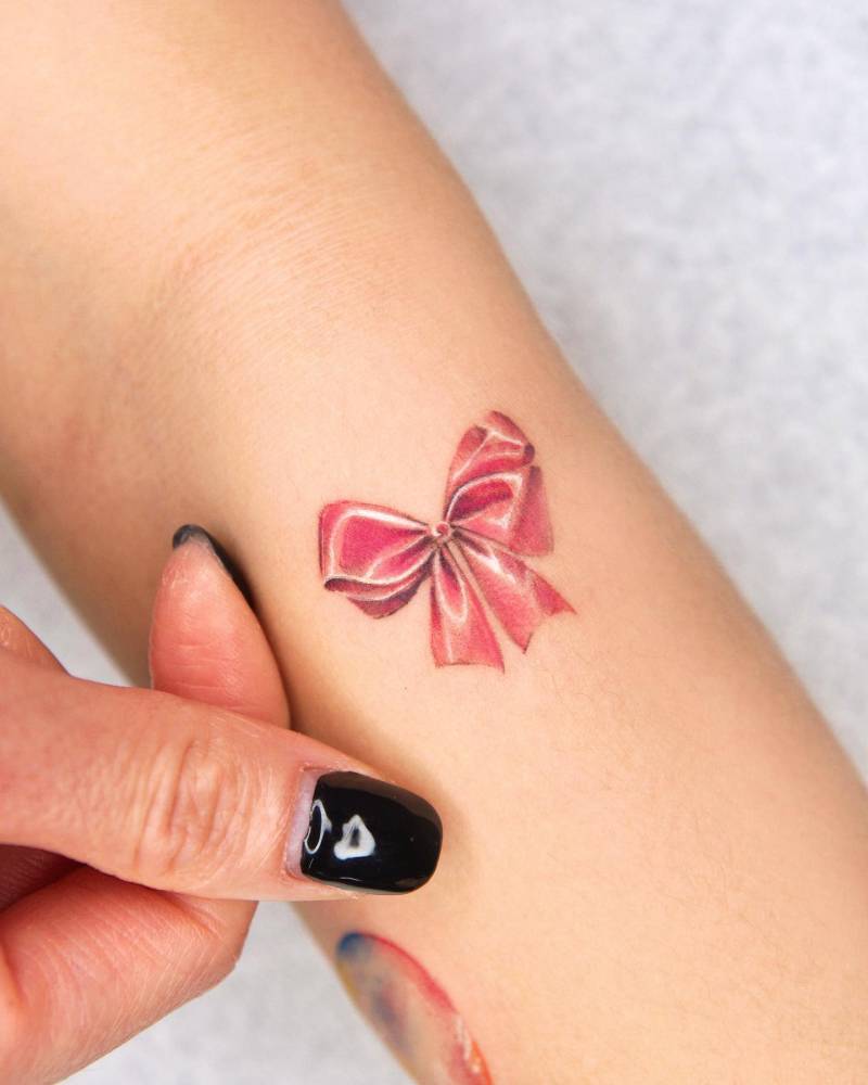 Micro-realistic style bow tattoo located on the forearm.