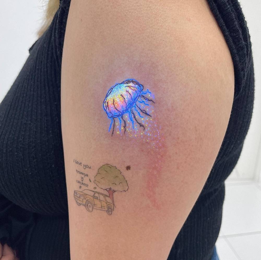 UV ink jellyfish tattoo in illustrative style placed on the upper arm.