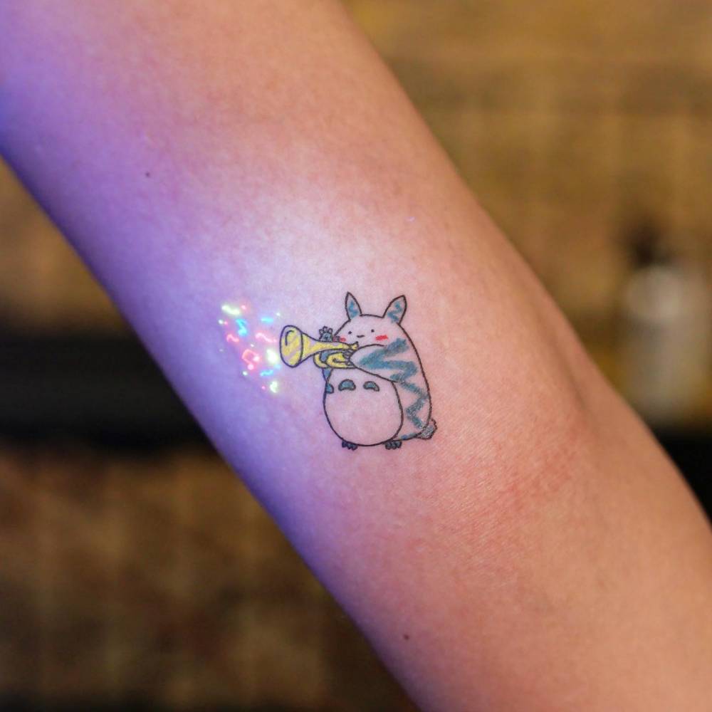 Totoro playing the trumpet tattooed on the inner arm.
