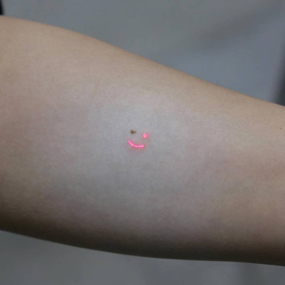 Tiny smiley face tattoo in minimalistic style located on the inner forearm.