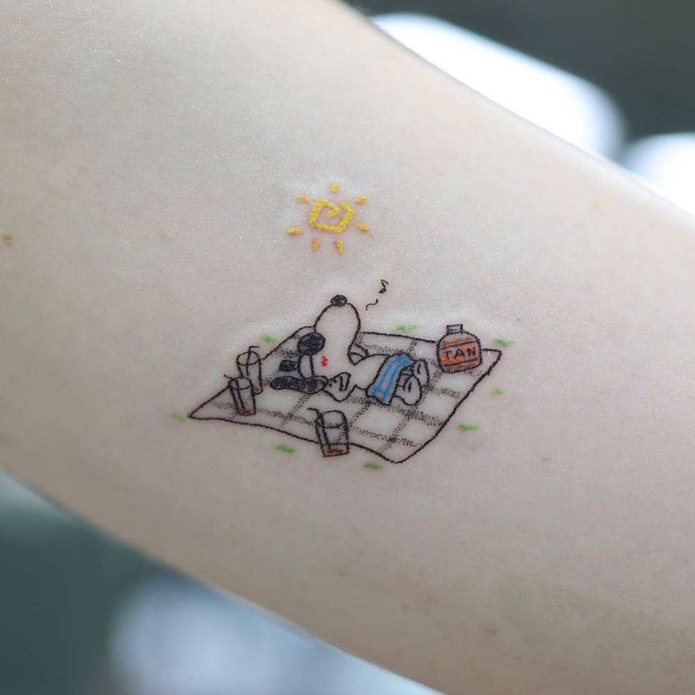 Relaxing Snoopy tattooed on the inner arm, cartoon style.