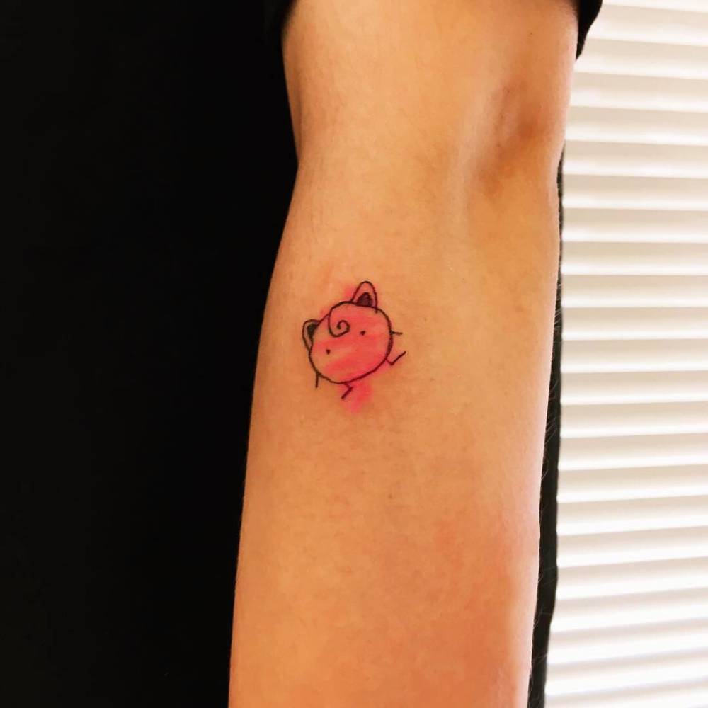 Small Jigglypuff tattoo located on the forearm, cartoon style.