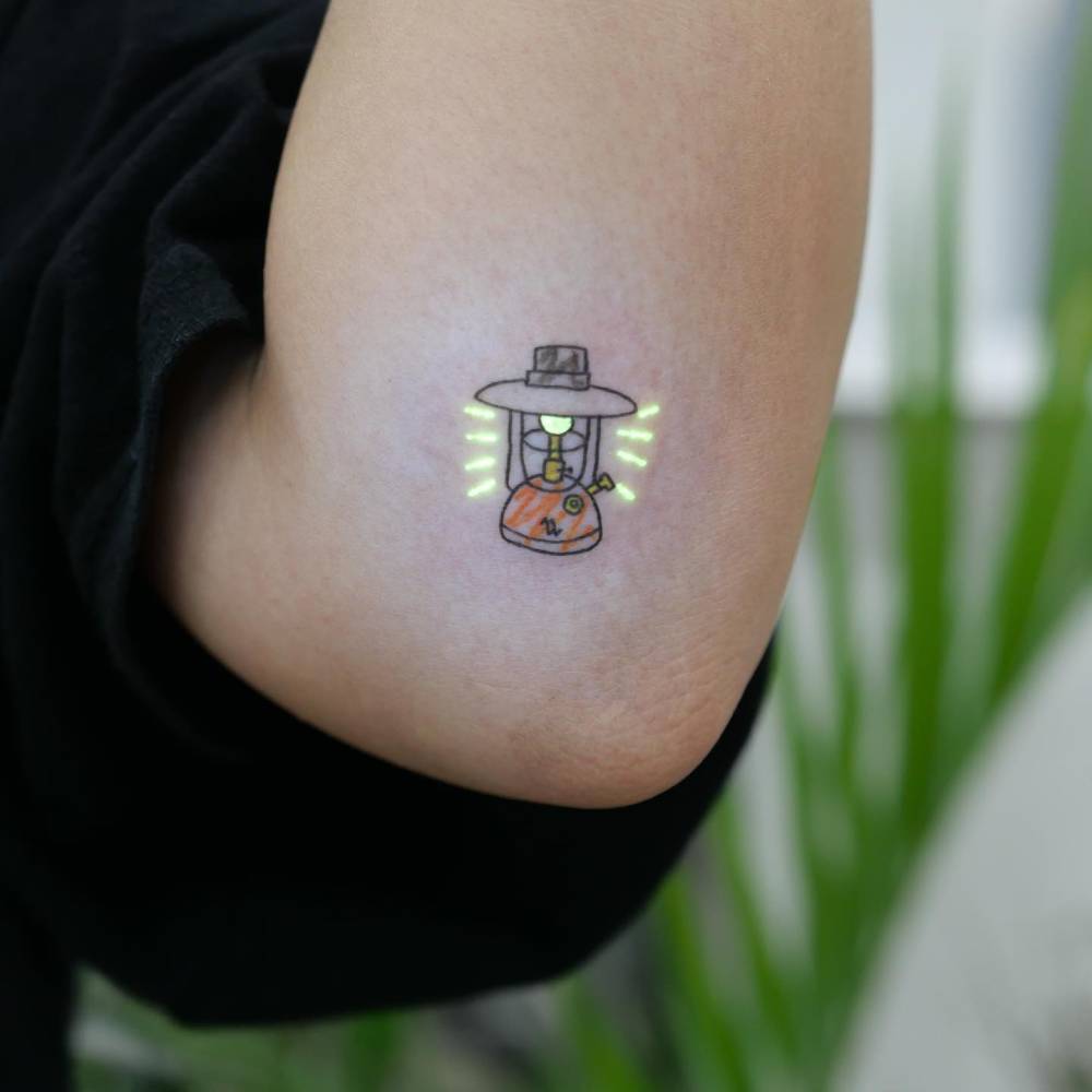 Tiny lantern tattoo in illustrative style located on the elbow.