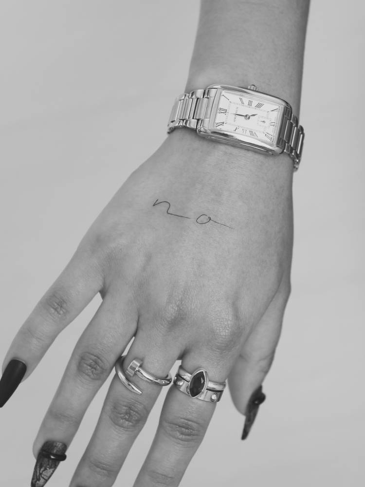 Handwritten font initials tattoo located on the hand.