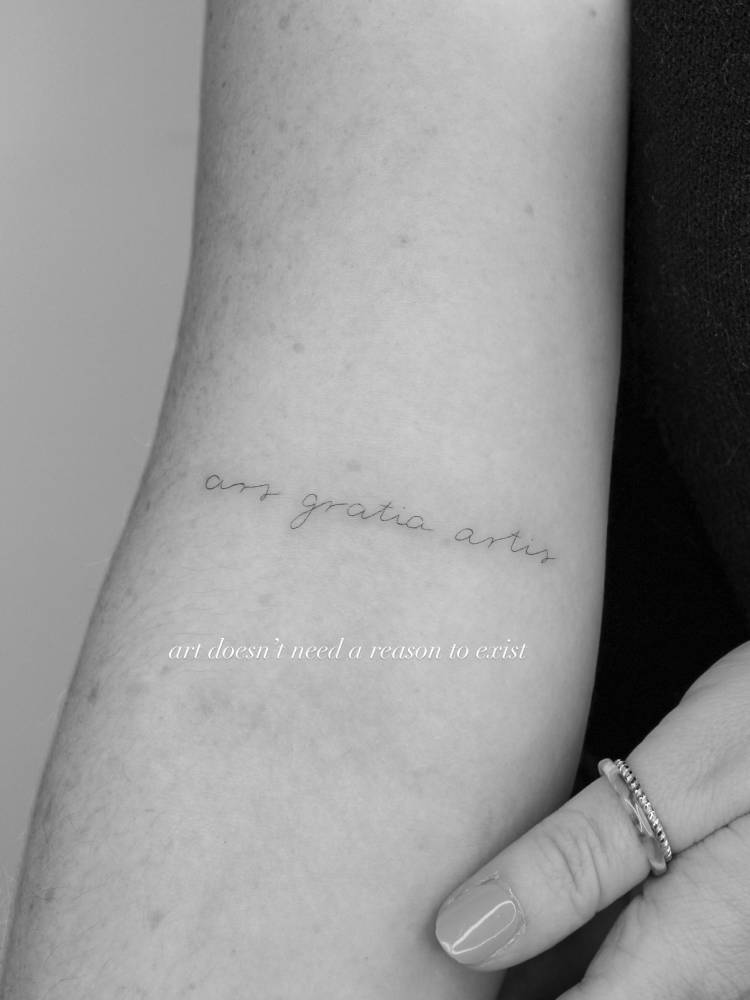 "Ars gratia artis" lettering tattoo handwritten on the bicep.