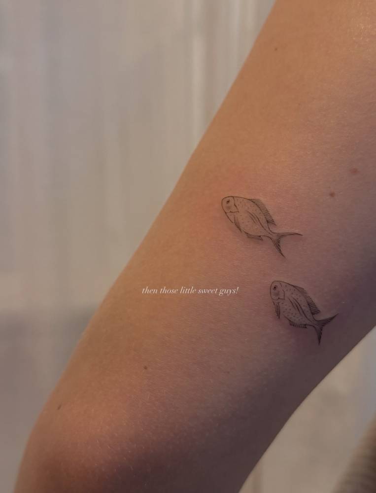 Fish tattoo in fine line style placed on the tricep.