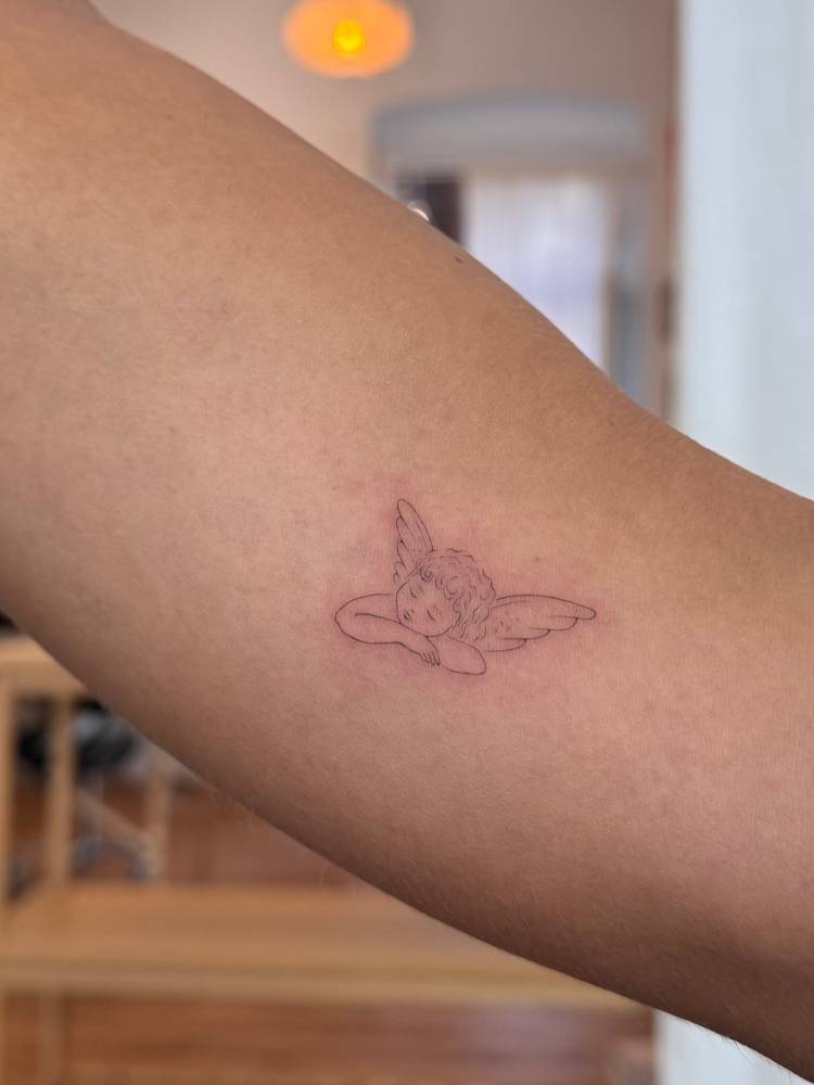 Sleeping cherub tattoo in fine line style located on the inner arm.