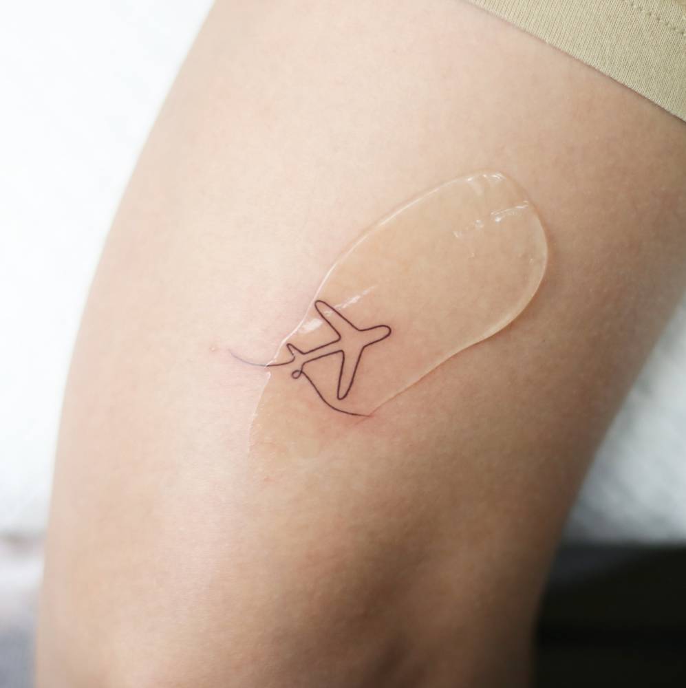 One line airplane and wave tattoo located on the tricep, minimalistic style.
