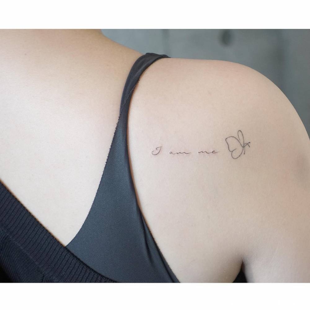"I am me" and butterfly tattoo located on the shoulder blade.