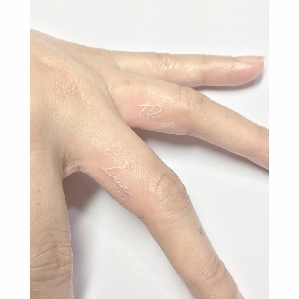 White ink initials tattoo located on the fingers.