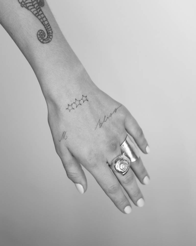 Stars, letter "M" and word "bliss" tattooed on the hand.