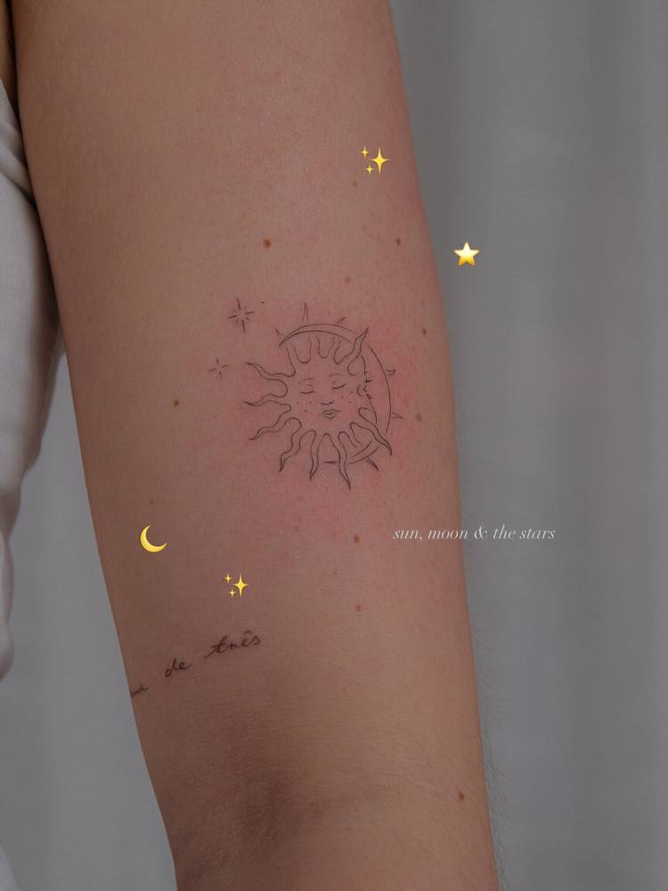 Sun and moon face tattooed on the upper arm, fine line style.