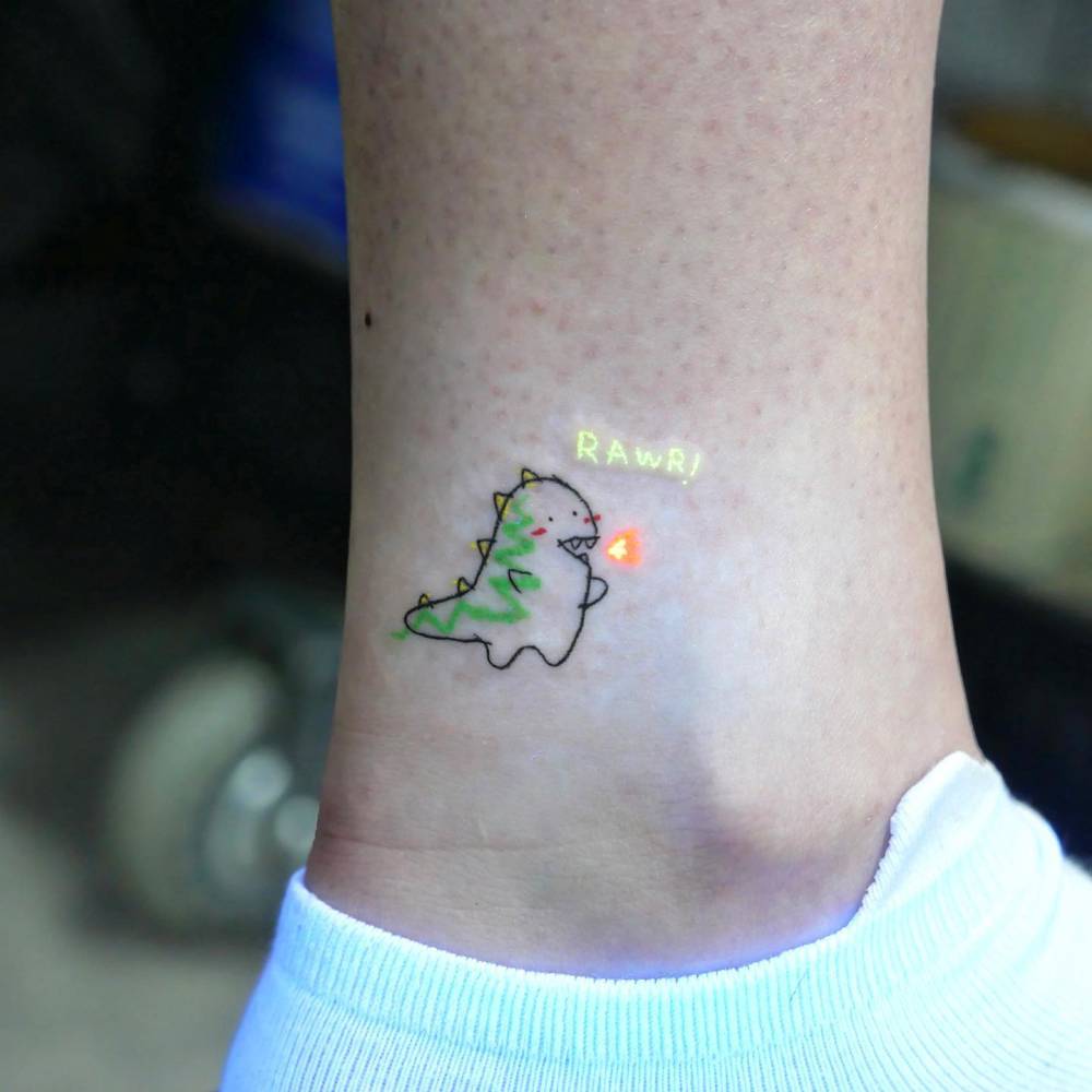 Cartoon style dinosaur tattoo located on the ankle.