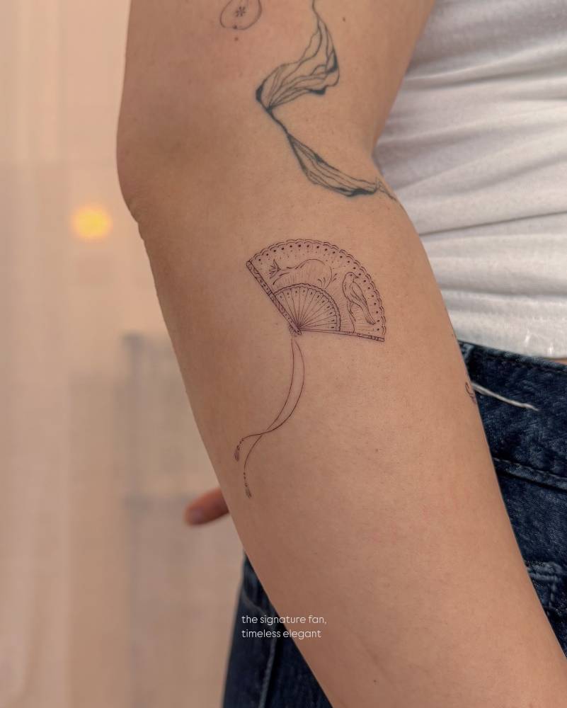 Little hand fan tattoo located on the forearm, fine line style.