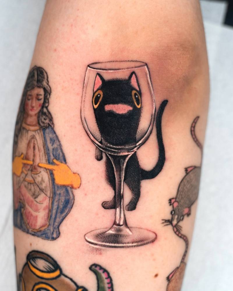 Pop art style black cat and wine glass tattoo placed on the elbow.