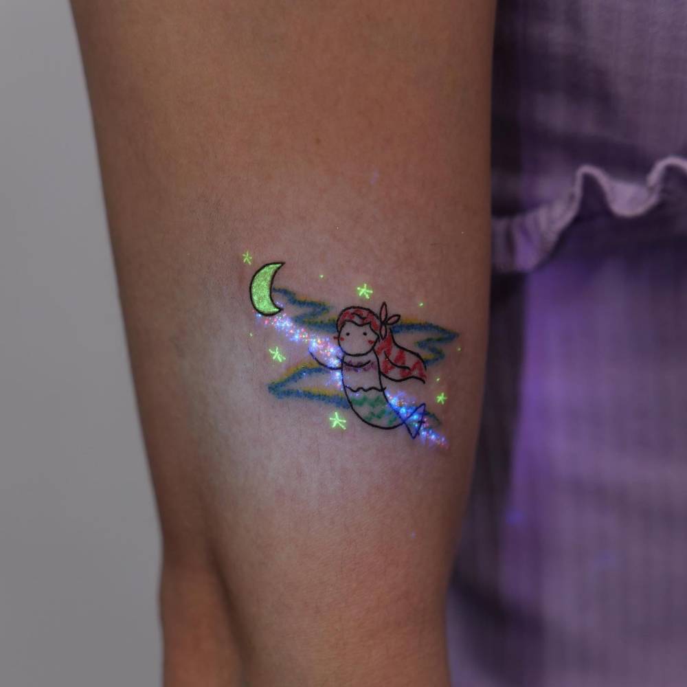 Cartoon style cute Ariel tattoo located on the upper arm.