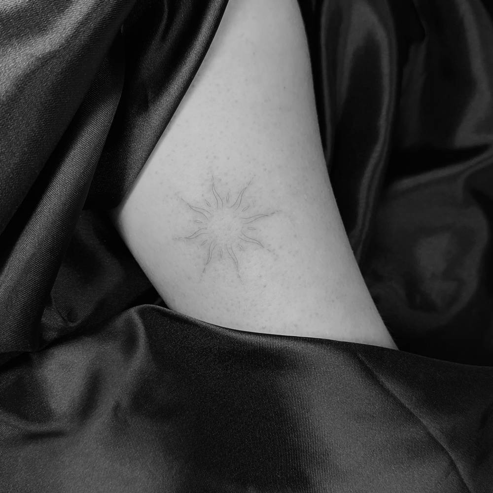 Sun tattoo in fine line style located on the inner forearm.