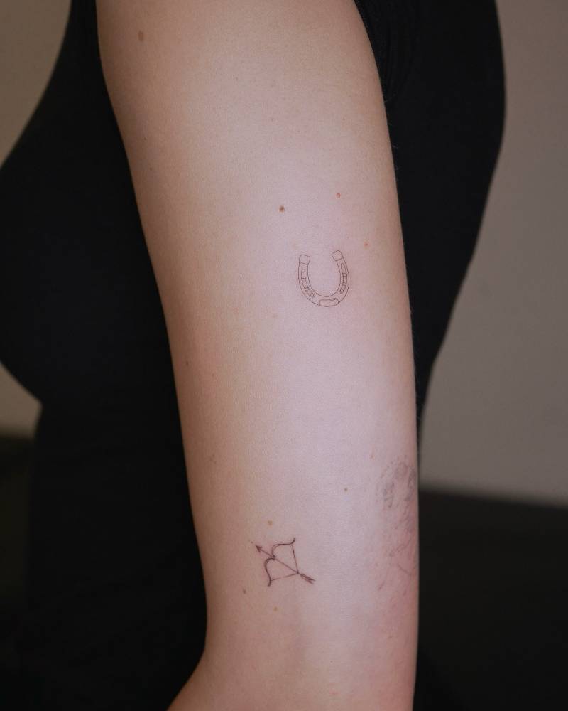 Fine line style horseshoe and bow and arrow tattoos.