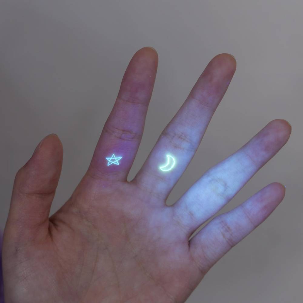 UV ink moon and star tattoo in minimalistic style located on the finger.
