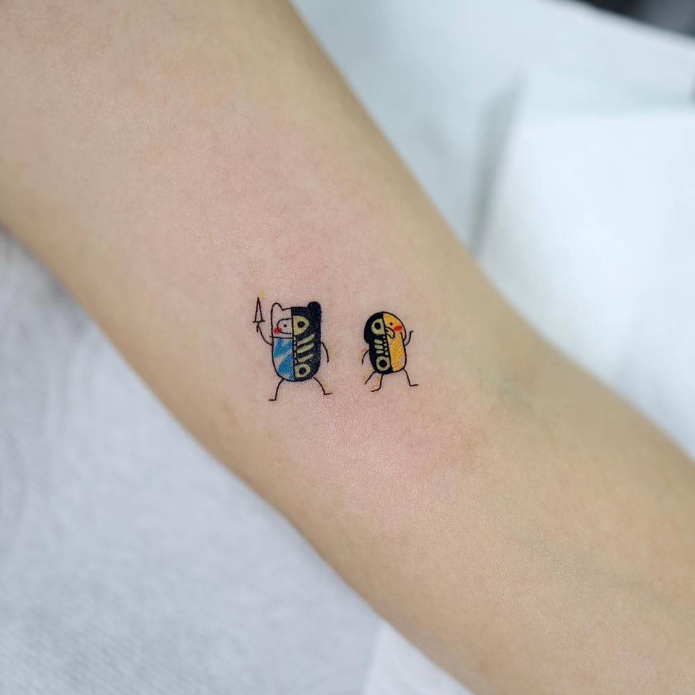 Finn and Jake tattoo in cartoon style done on the inner arm.