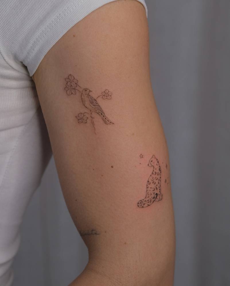 Fine line style bird on a branch tattoo located on the upper arm.