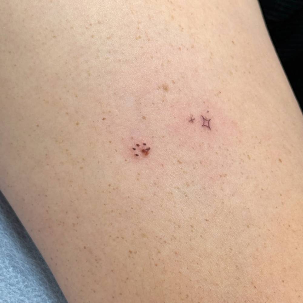 Minimalistic style paw print birthmark cover up and little stars tattooed on the upper arm.