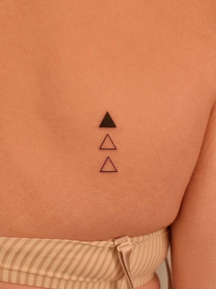 Three small triangles in minimalistic style tattooed on the shoulder blade.