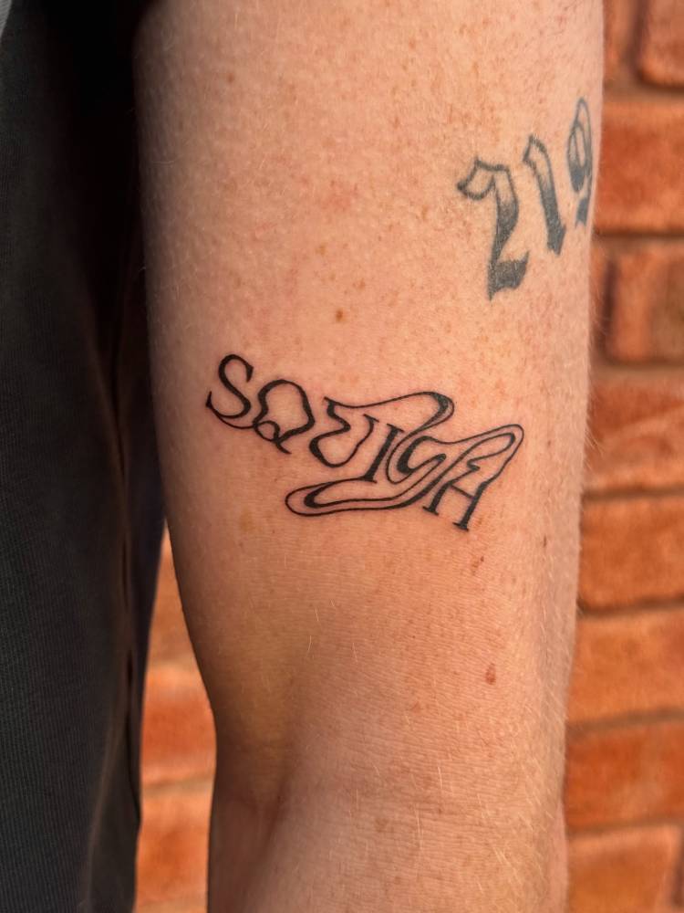 Abstract style word "squish" tattoo located on the upper arm.