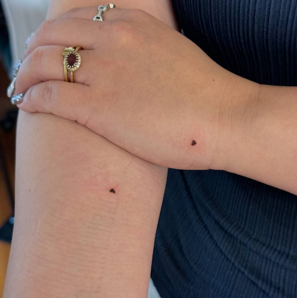 Minimalistic hearts tattooed on the hand and upper arm.