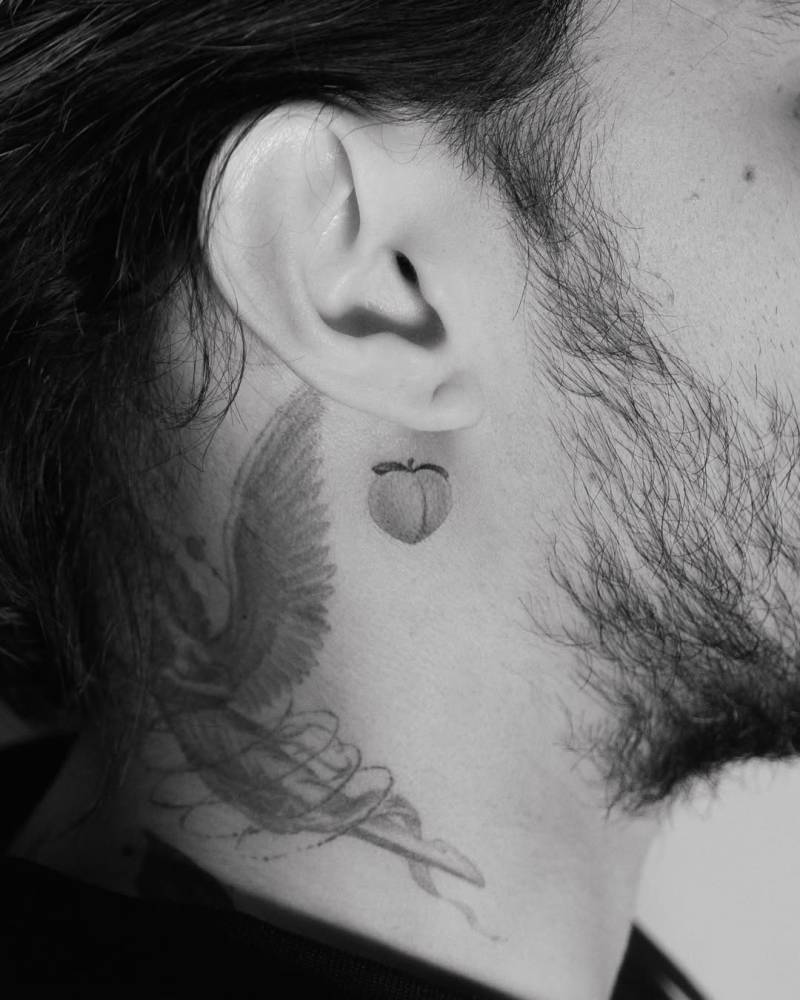 Tiny micro-realistic peach tattoo placed behind the ear.
