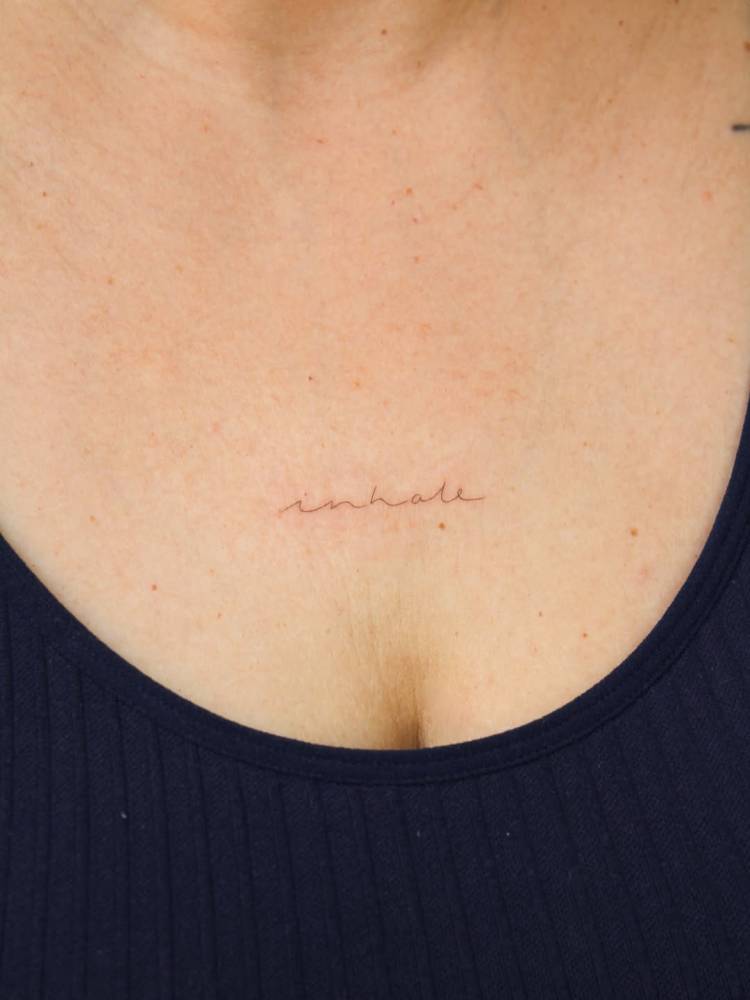 Handwritten font word "inhale" tattooed on the sternum.