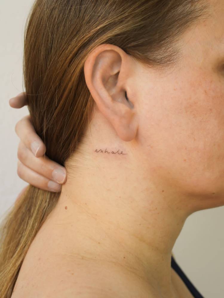 Lettering tattoo of the word "exhale" located behind the ear.