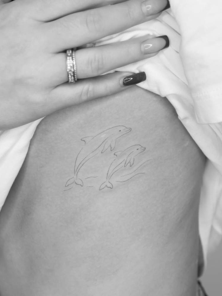 Little dolphins tattoo in fine line style placed on the rib.