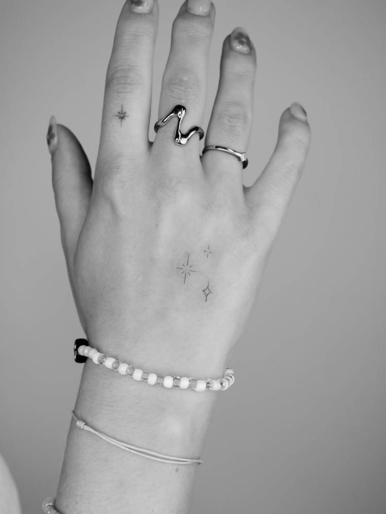 Minimalistic sparkling stars tattoo located on the hand.