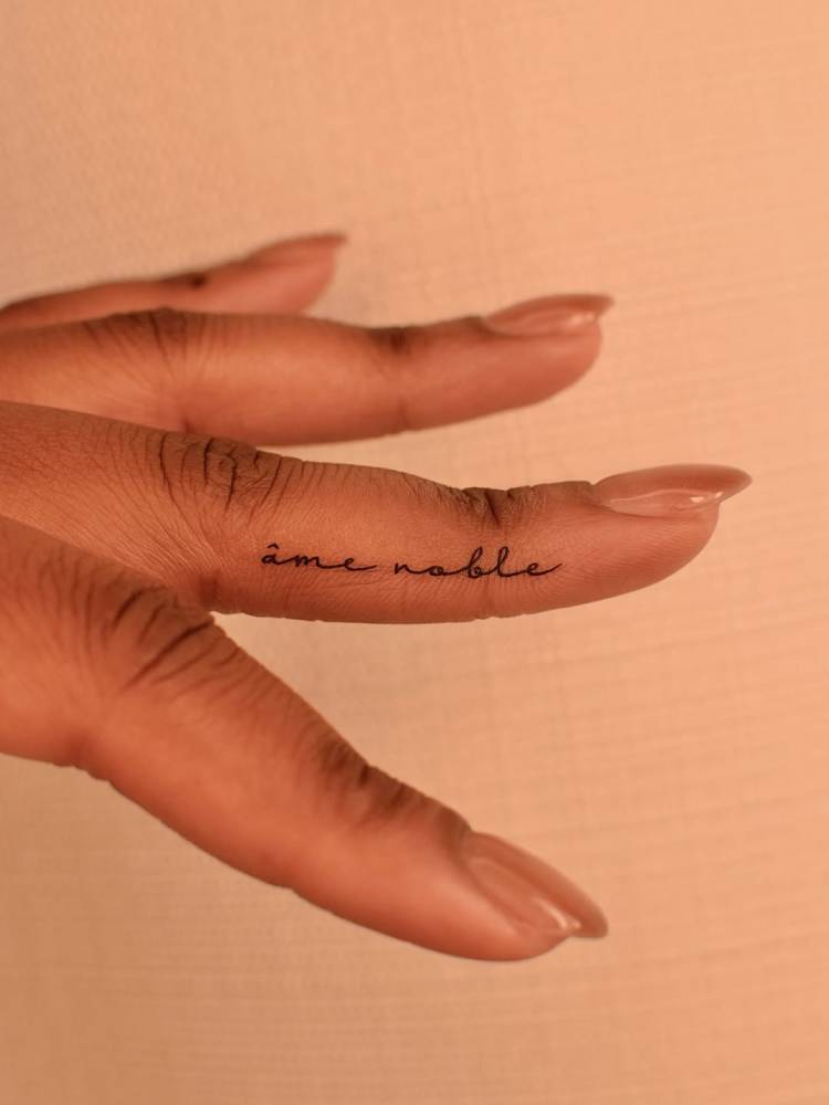 "Âme noble" in handwritten font tattooed on the finger.