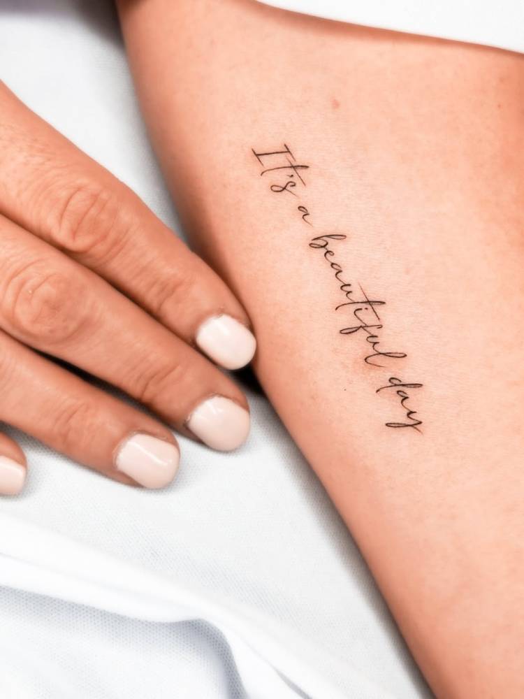 "It's a beautiful day" lettering tattoo located on the inner arm.