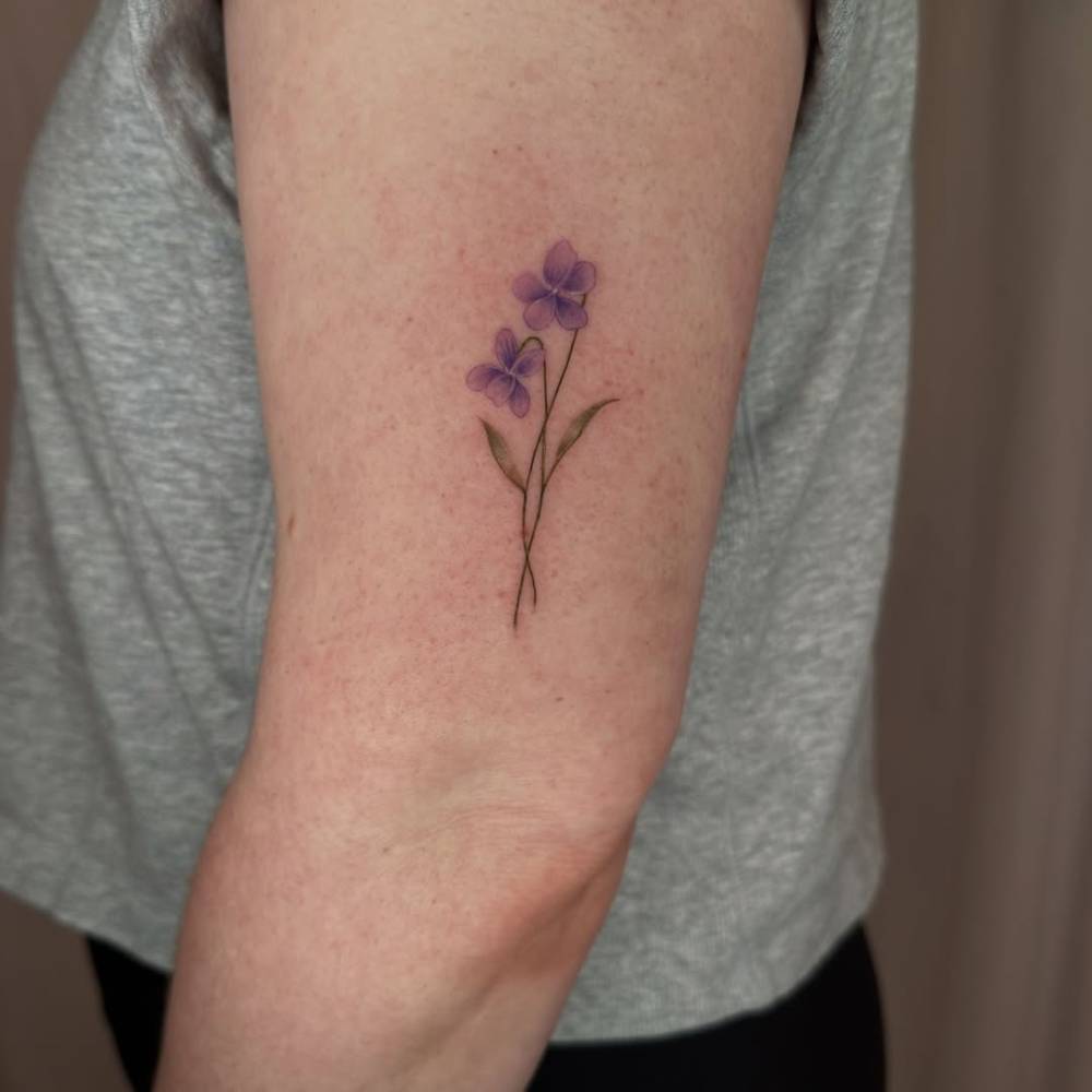 Watercolor style violet flowers tattoo done on the upper arm.