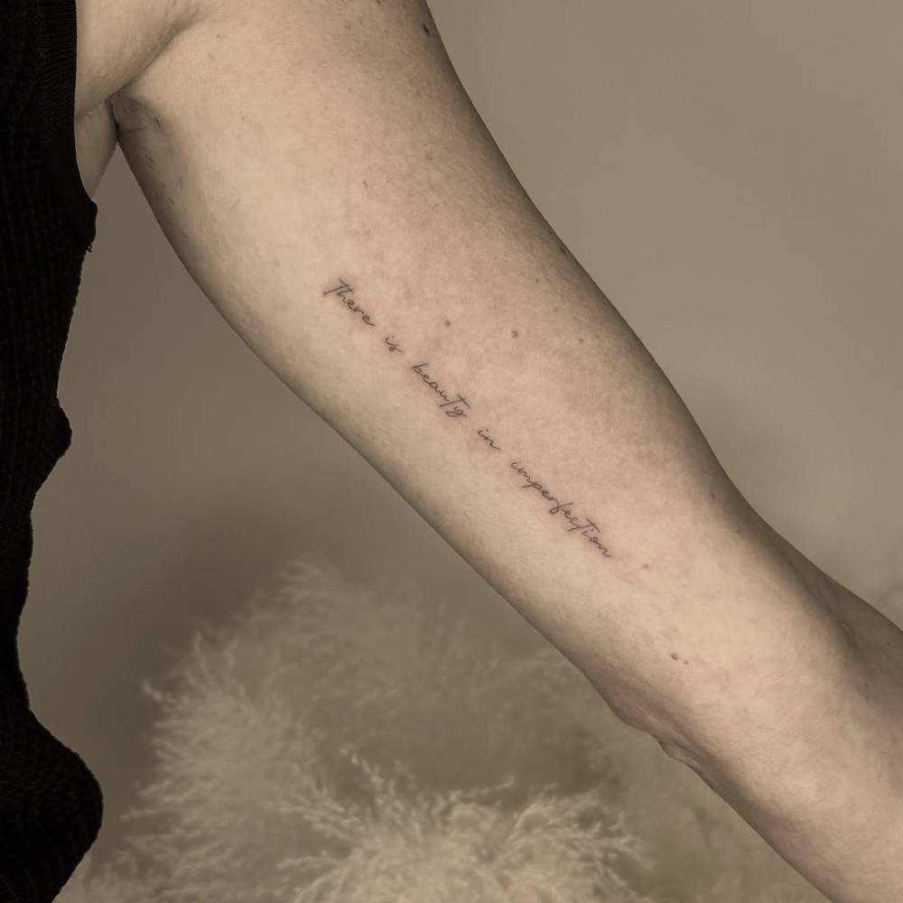 "There is beauty in imperfection" lettering tattoo placed on the inner arm.