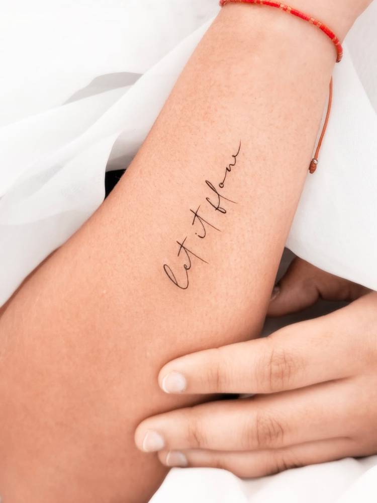 "Let it flow" lettering tattoo located on the wrist.