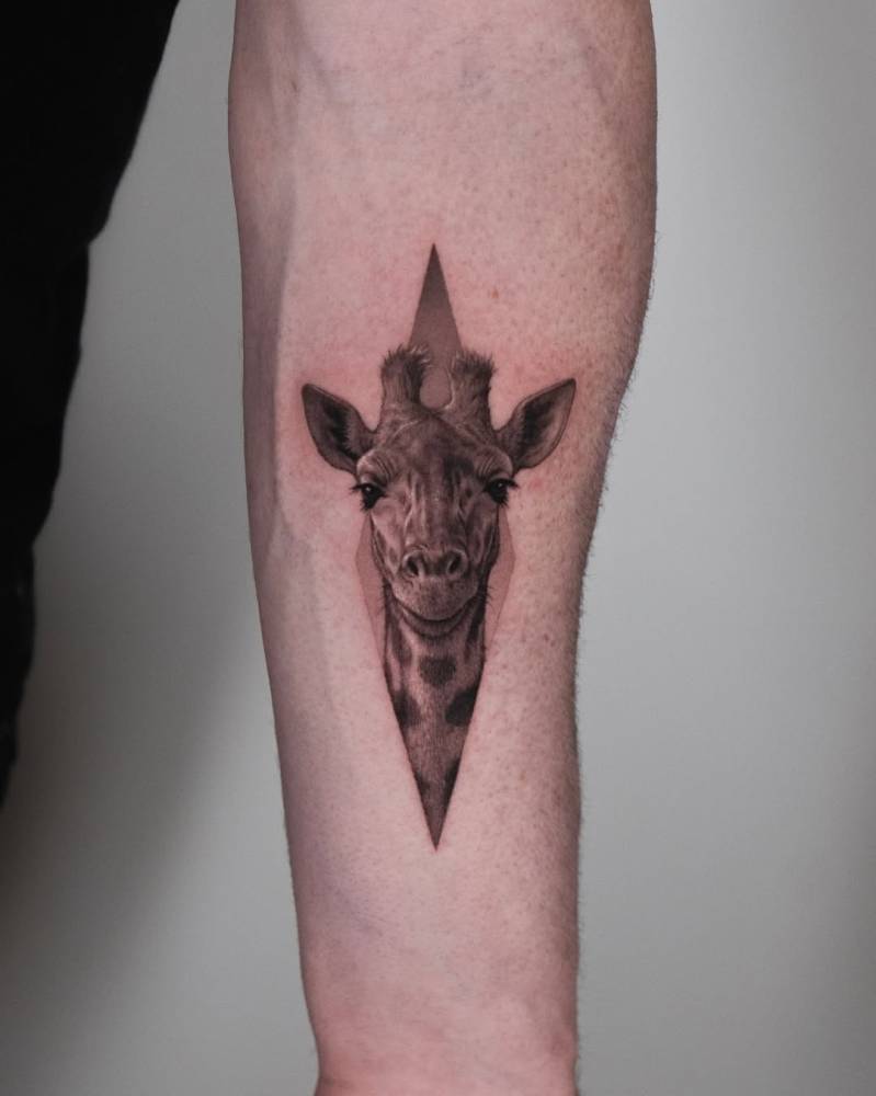 Giraffe portrait tattoo in black and grey style located on the inner forearm.