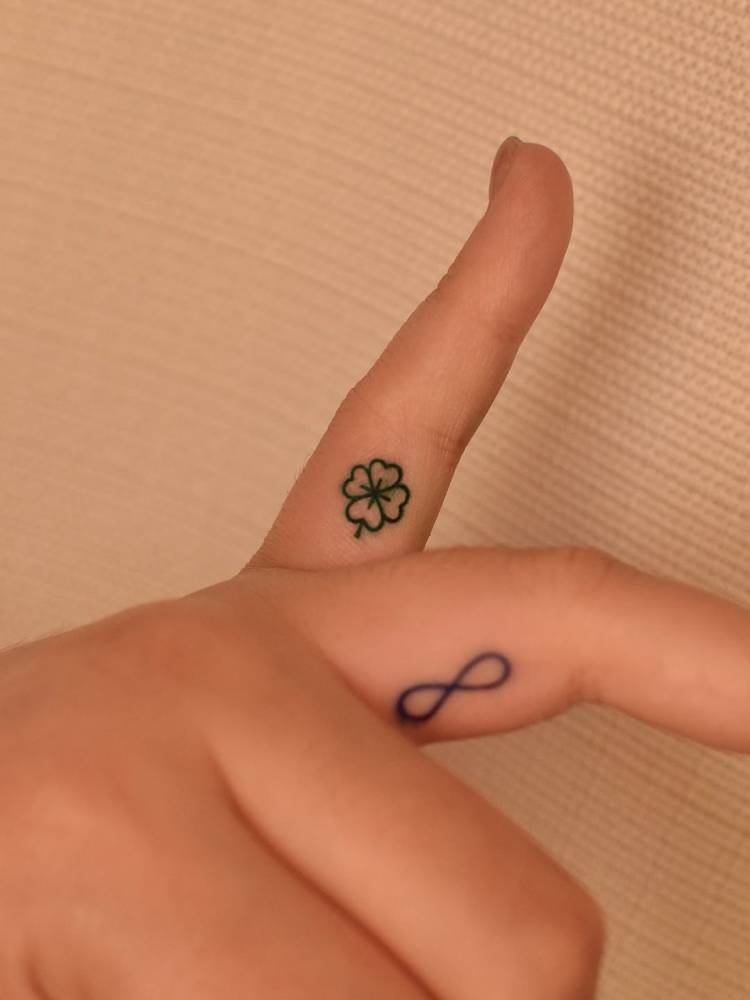 Green four leaf clover tattoo in minimalistic style located on the finger.