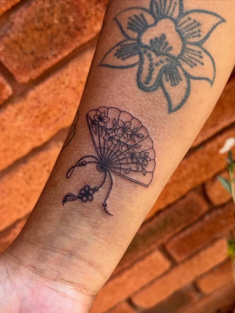 Hand fan tattoo in fine line style placed on the wrist.