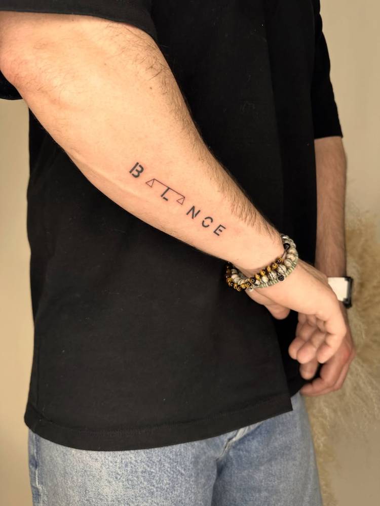 Lettering tattoo of the word "balance" located on the forearm.