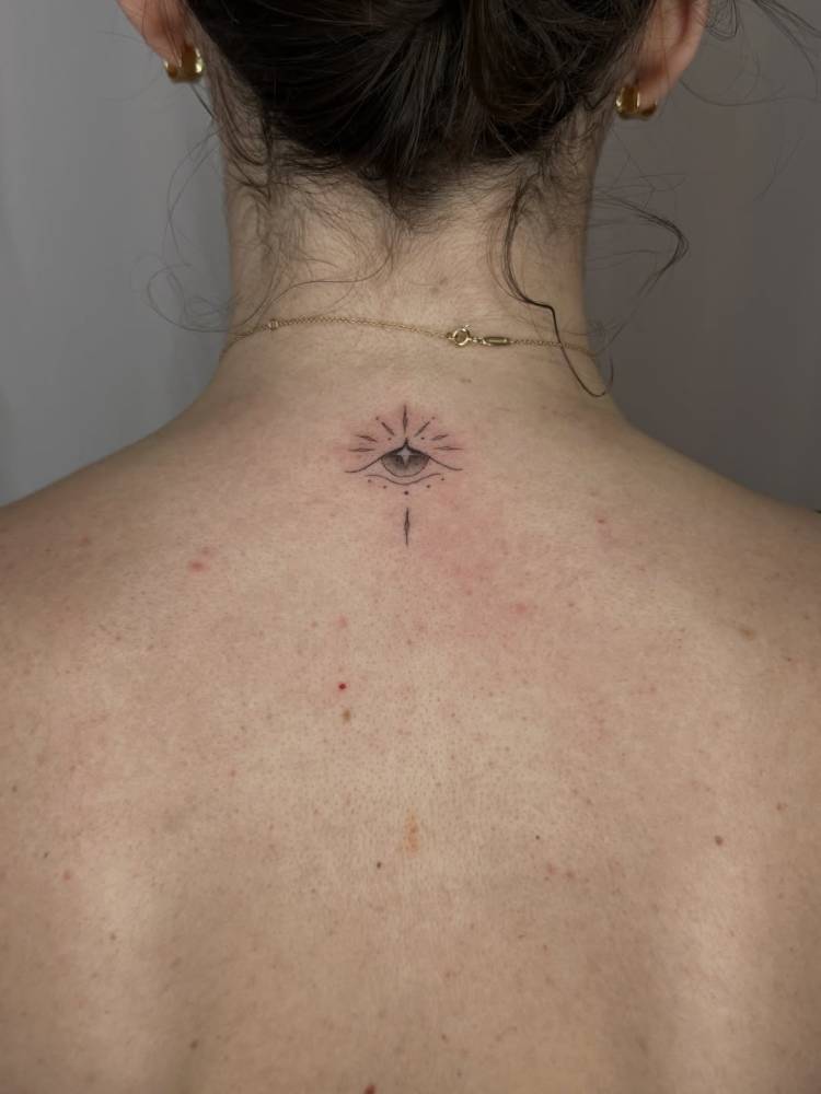 Evil eye tattoo in illustrative style located on the upper back.
