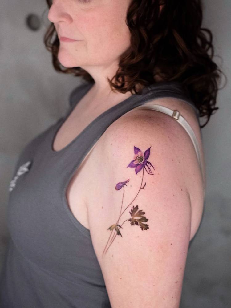 Columbine flower tattoo in watercolor style located on the upper arm.