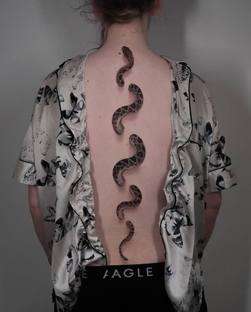 Snake tattoo located on the spine, done in black and grey style.