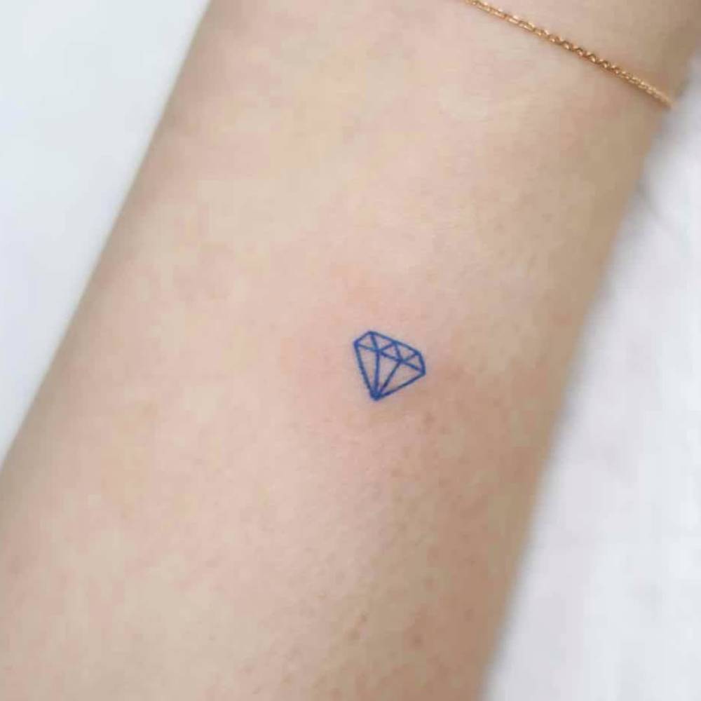 Tiny minimalistic blue diamond tattoo located on the wrist.