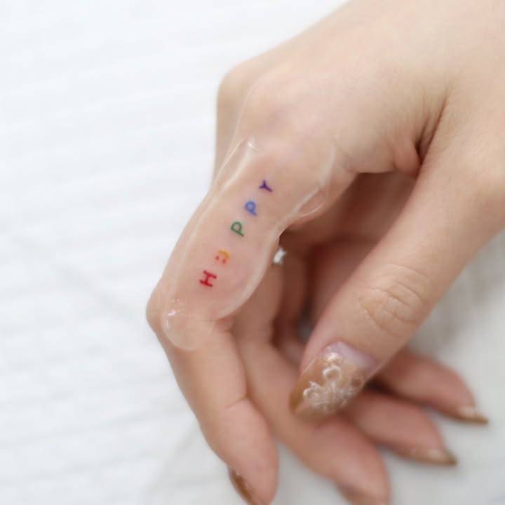Colorful lettering tattoo of the word "happy" done on the finger.