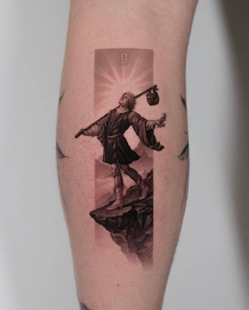 The Fool tarot card tattooed on the calf, micro-realistic style.